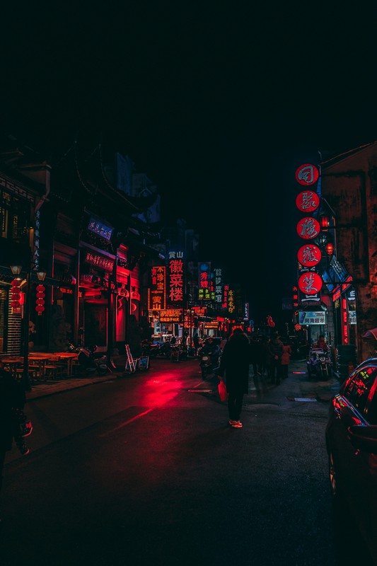 a street with neon signs and people walking on it mount huangshan