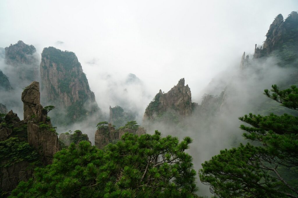 a foggy mountain range with trees with Huangshan in the background mount huangshan