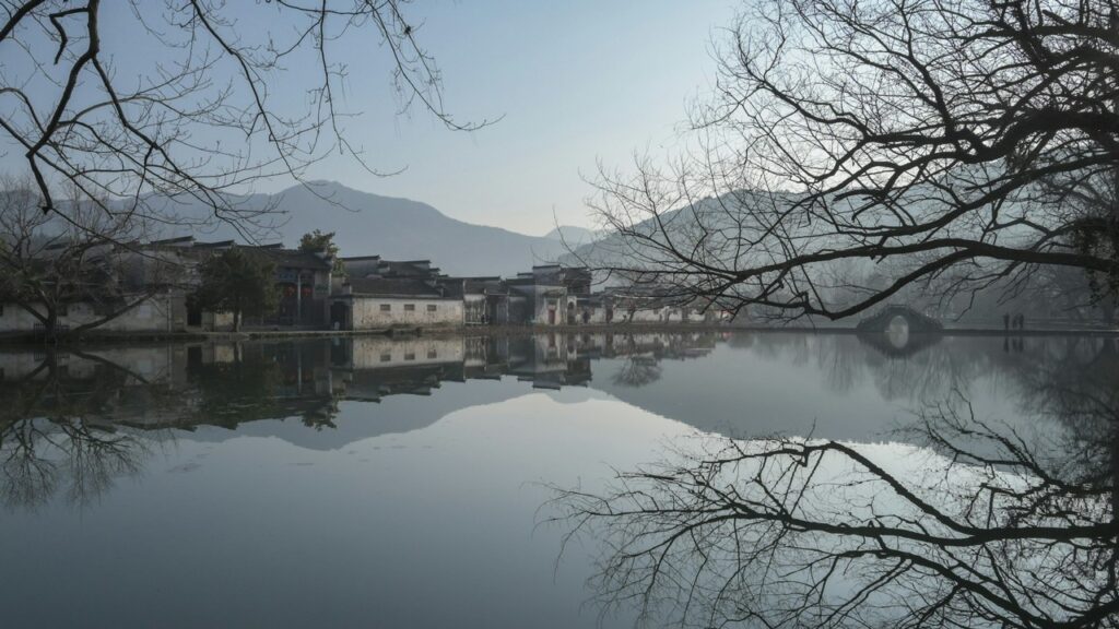 a body of water with buildings and mountains in the background mount huangshan weather