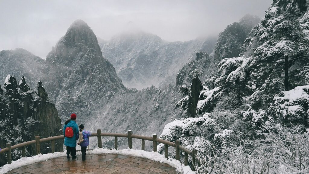 a group of people standing on a deck overlooking a snowy mountain yellow mountain china